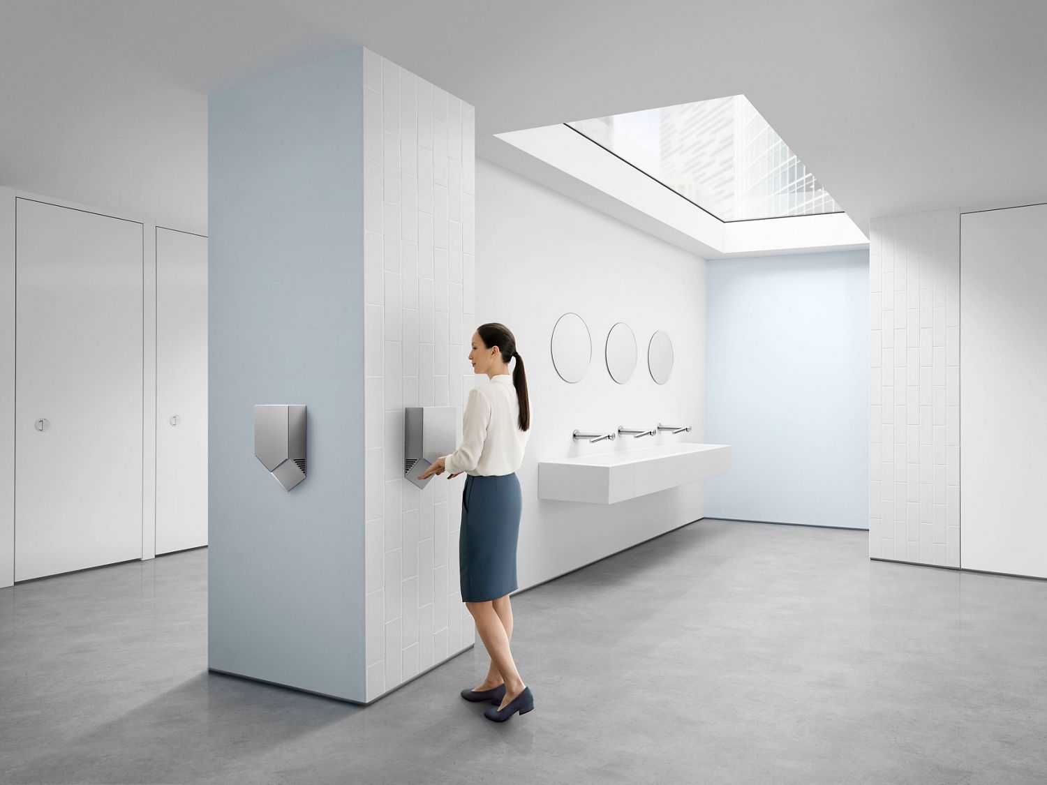 A woman uses the Dyson Airblade 9kj in a bathroom to dry her hands.